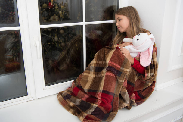 Christmas is here. Small child with rabbit toy at window. Small girl hold toy friend. Little child relax on Christmas eve. Little girl enjoy Christmas at home. Merry Christmas and happy new year - Photo, Image