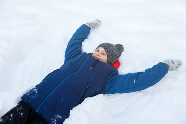 carino ragazzo in giacca blu gioca con la neve, si diverte, sorride. Teenager alza le mani, fa figure sulla neve nel parco invernale. Stile di vita attivo, attività invernale, giochi invernali all'aperto, palle di neve
 - Foto, immagini