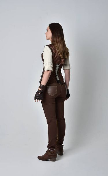 täyspitkä muotokuva brunette tyttö yllään ruskea nahka steampunk asu. seisova poseeraa kameran edessä harmaalla studiotaustalla
. - Valokuva, kuva
