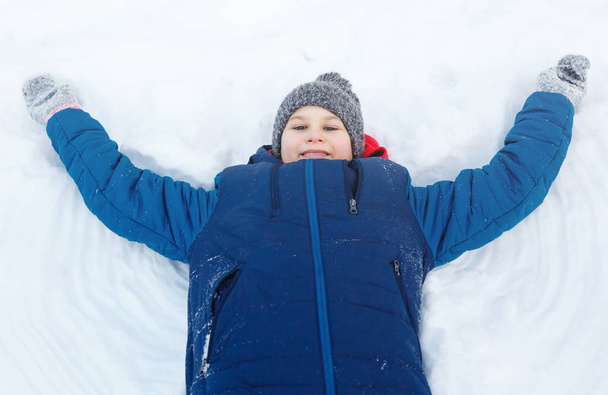 carino ragazzo in giacca blu gioca con la neve, si diverte, sorride. Teenager alza le mani, fa figure sulla neve nel parco invernale. Stile di vita attivo, attività invernale, giochi invernali all'aperto, palle di neve
 - Foto, immagini