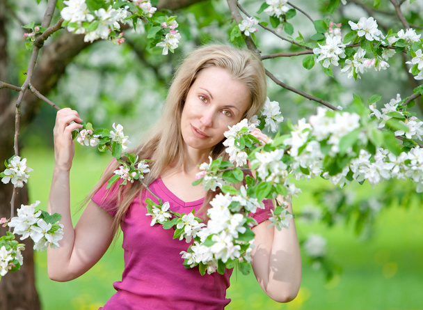 young attractive woman standing near the blossoming apple tree - Fotó, kép