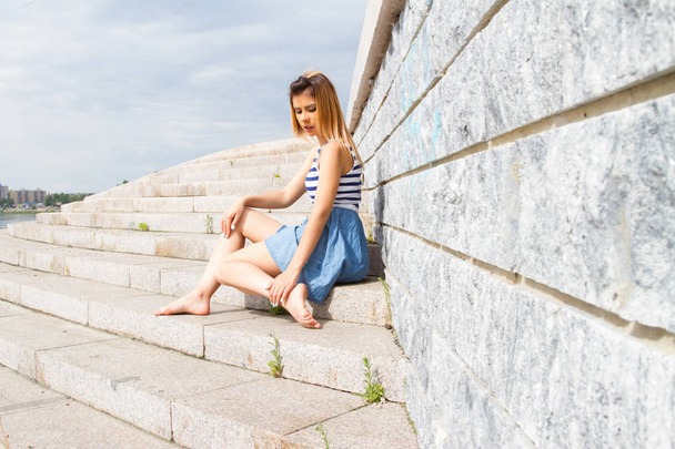 молода дівчина сидить на сходах бетонних сходів, спираючись на кам'яну стіну
 - Фото, зображення