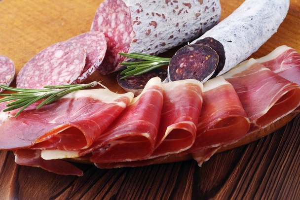 Delícias de carne de close-up, fatias finas de jamon e salsicha italiana em uma tábua de madeira
. - Foto, Imagem
