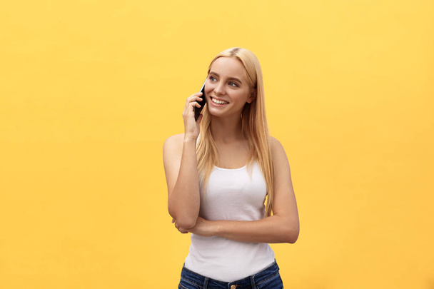 Image of gorgeous woman in casual being surprised or excited to receive pleasant talk on her cell phone, over yellow background - 写真・画像