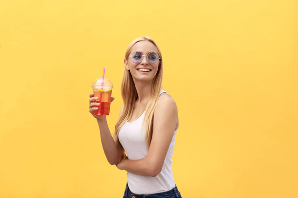 黄色の背景に分離されたジュースのガラスを押しながら白い t シャツを着てサングラスで素敵な女性 - 写真・画像
