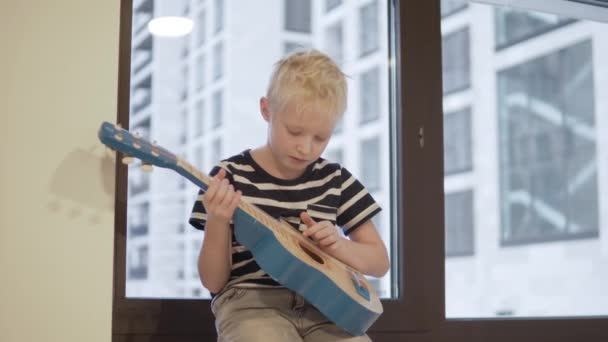 Ein trauriger Junge mit einer Gitarre sitzt am Fenster - Filmmaterial, Video
