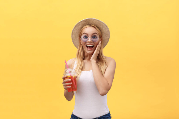 Mesés nő napszemüveget visel fehér póló, rövid idő tárolás a pohár gyümölcslé izolált át a sárga háttér - Fotó, kép