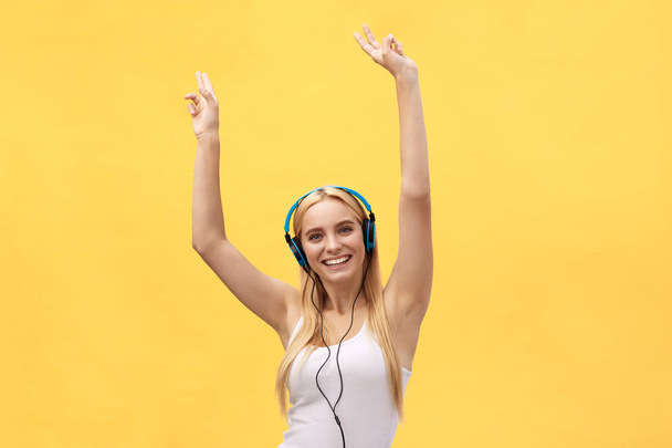 Lifestyle Concept: Portret van een blije vrouw in wit t-shirt en luisteren naar muziek met koptelefoon terwijl dansen en zingen geïsoleerd op gele achtergrond - Foto, afbeelding