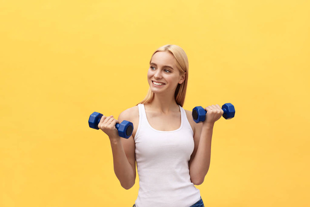 Fitness-Frau hebt Gewichte und lächelt glücklich vereinzelt auf gelbem Hintergrund. fit sportliche kaukasische weibliche Fitness-Modell. - Foto, Bild