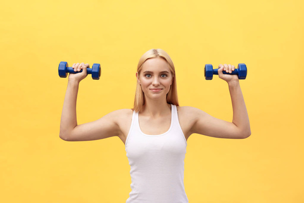 Fitness-Frau hebt Gewichte und lächelt glücklich vereinzelt auf gelbem Hintergrund. fit sportliche kaukasische weibliche Fitness-Modell. - Foto, Bild
