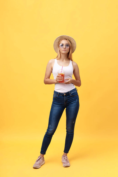 Ganzkörperporträt einer fröhlichen jungen Frau, die Sommerkleidung trägt, während sie posiert und die Kamera isoliert über gelbem Sommerhintergrund betrachtet - Foto, Bild
