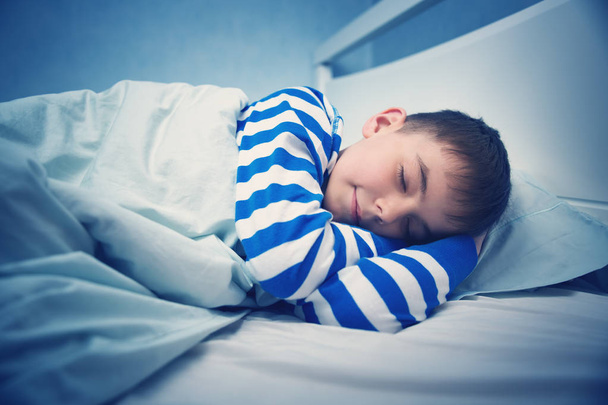 Boy sleeping in bed in pajamas. Child lying in bed on pillow at night - Photo, image