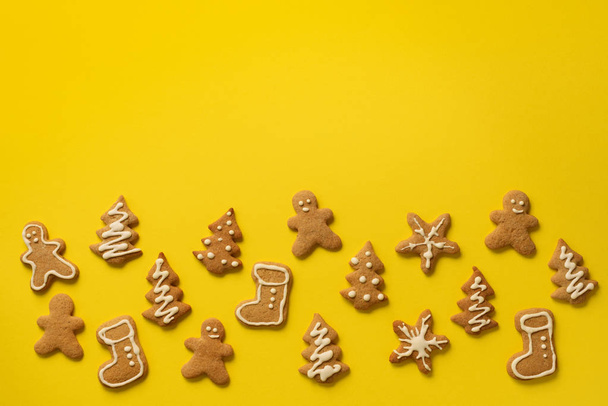 Christmas handmade cookies on yellow background with copy space. Pattern of gingerbread men, snowflake, star, fir-tree, boot shapes. New year concept. - Zdjęcie, obraz