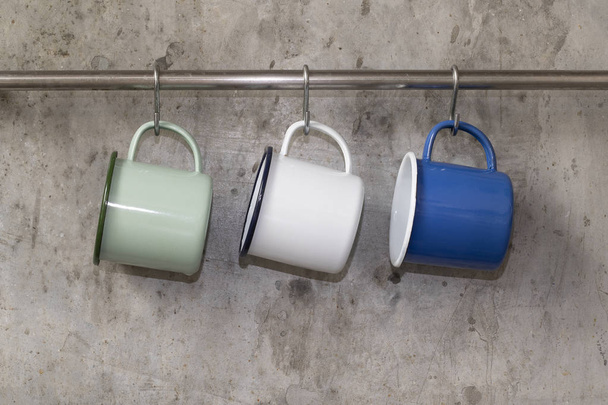 Tin cups hanging on stainless rail on cement wall background. - 写真・画像
