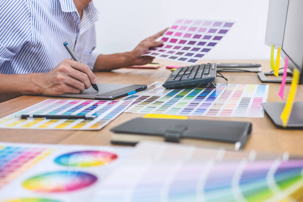 Imagen del diseñador gráfico creativo masculino que trabaja en la selección de colores y dibuja en la tableta gráfica en el lugar de trabajo con herramientas de trabajo y accesorios en el espacio de trabajo. - Foto, imagen