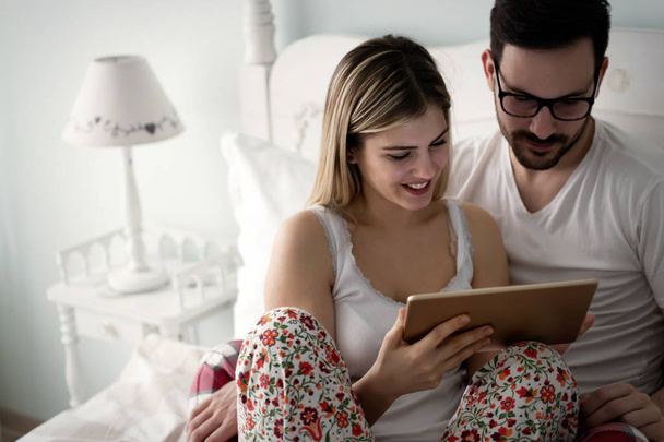 Young attractive couple using digital tablet in bedroom - 写真・画像