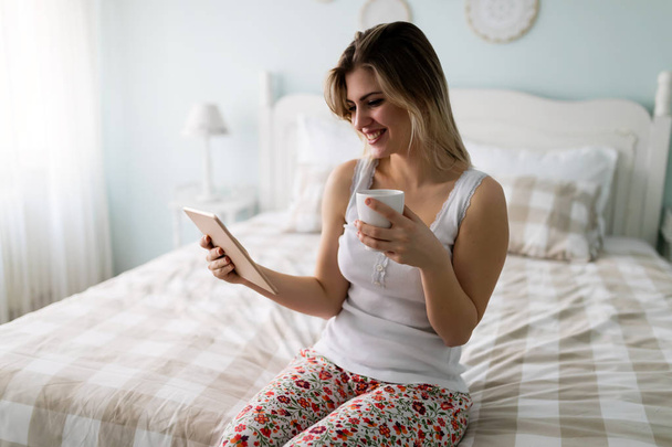 Beautiful young woman using digital tablet in bed - Foto, afbeelding