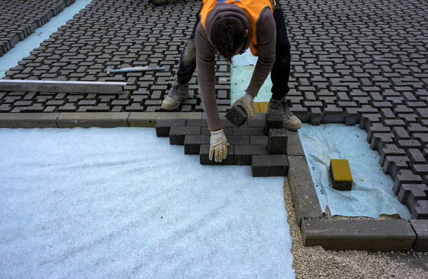 Stavební dělník pokládající propletený dlažební beton na prostěradlo netkané podestýlky z písku a upevňující je na místo. - Fotografie, Obrázek