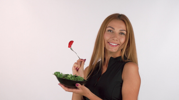 Beautiful sportswoman holding a bowl of salad, smiling to the camera - Photo, Image