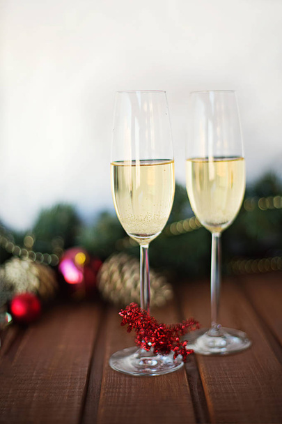 two New Year's glasses with champagne wine on a wooden table  a white background and branches of a decorated Christmas tree - Foto, immagini