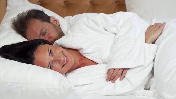Cheerful mature woman going to sleep lying in the bed with her husband - Photo, Image