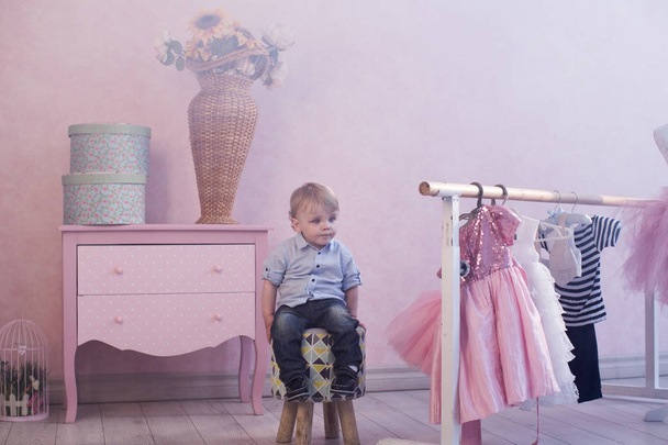 little caucasian boy sitting on chair posing to camera at home with pink walls - Foto, Bild