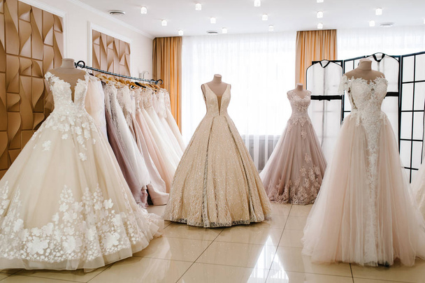 Beautiful wedding dresses, bridal dress hanging on hangers and mannequin in studio. Fashion look. Interior of bridal salon. - Фото, изображение