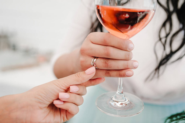 A photo of lady holding a glass of wine with a wedding ring on finger on party. Girl, woman standing in the background and drink wine. Concept of celebrate, holiday. - Foto, imagen