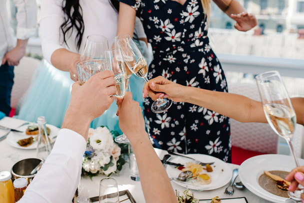 Cheers! People celebrate and raise glasses of wine for toast. Group of man and woman cheering with sparkling champagne and whiskey, scotch, whisky, brandy in rooftop restaurant overlooking the city. - Foto, imagen