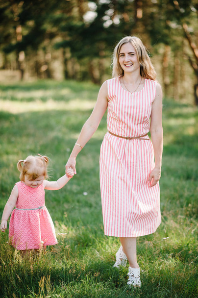 The mother runs with a daughter and holds her hand on nature on summer day,  vacation. Mom and girl walking and playing in the park at the sunset time. Concept of friendly family. Close Up. - Фото, изображение