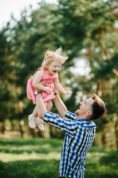 The father throws up and spins the daughter on nature on summer day vacation. Dad and girl playing in the park at the sunset time. Girl flying. Concept of friendly family. Closeup. - Foto, imagen