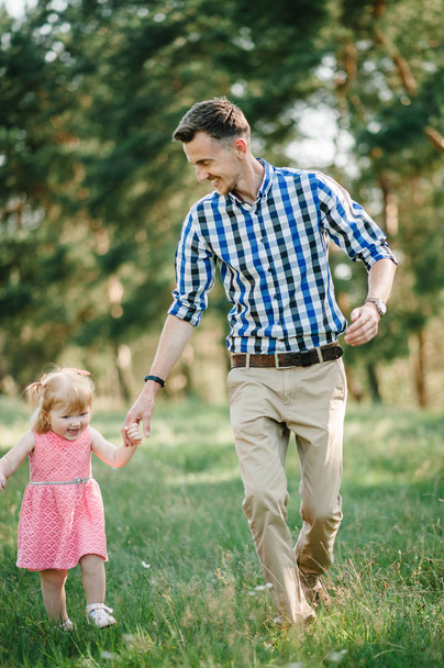 The father runs with a daughter and holds her hand on nature on summer day vacation. Dad and girl walking and playing in the park at the sunset time. Concept of friendly family. Closeup. - Foto, Imagem