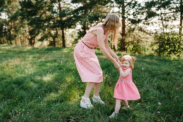 Jonge moeder met plezier met dochter in groen park - Foto, afbeelding