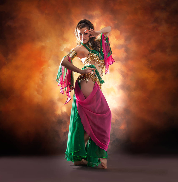 Gorgeous woman bellydancer dancing in traditional bellydance costume over colored studio background. - Foto, afbeelding