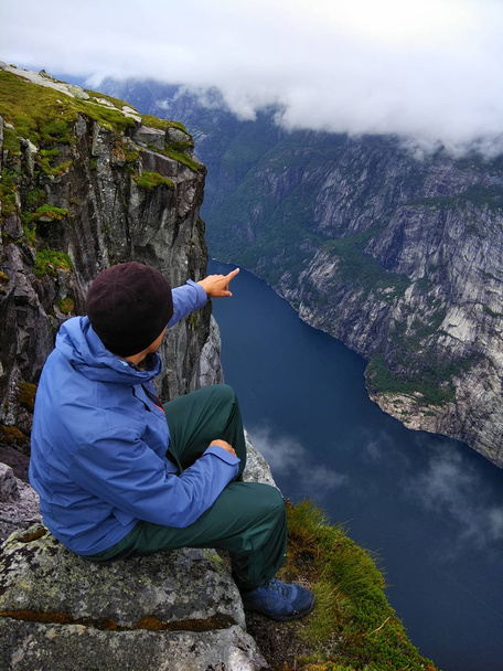 Mann sitzt am Rand einer Klippe über dem Lysefjord, auf dem Weg nach Kjeragbolten, Norwegen - Foto, Bild