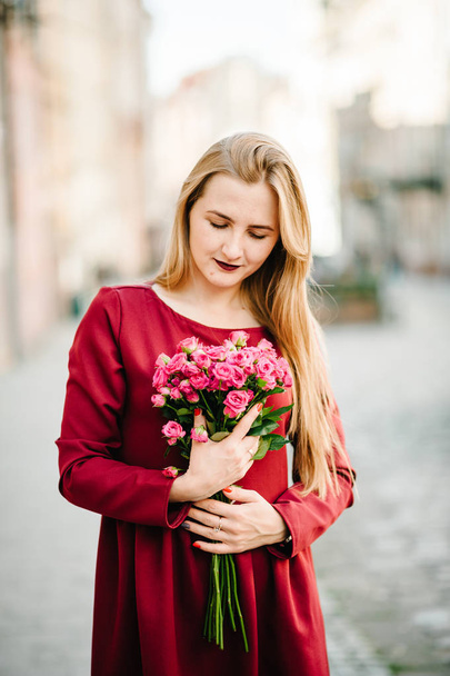 Portrait of young stylish woman in red dress holding bouquet of pink roses  - Foto, afbeelding