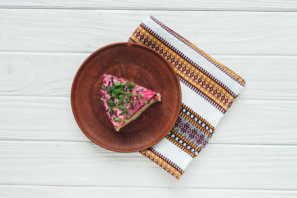 top view of tasty traditional russian salad on plate with embroidered towel on white wooden background - Photo, Image