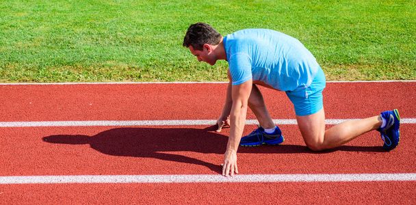 Make effort for victory. Adult runner prepare race at stadium. How to start running. Sport motivation concept. Man athlete runner stand low start position stadium path sunny day. Runner ready to go - Foto, afbeelding