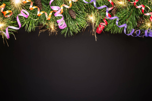 Weihnachts- oder Neujahrsrand mit Tannenzweigen und festlichen Luftschlangen auf schwarzem Hintergrund - Foto, Bild