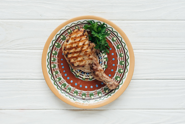vista superior del filete de carne de costilla a la parrilla en plato con perejil sobre fondo de madera blanco
 - Foto, Imagen