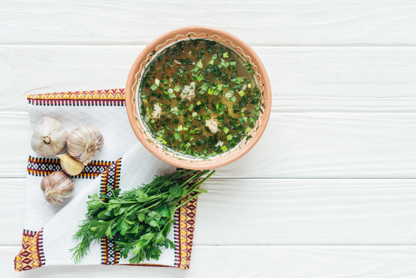 vista superior de la sopa de pescado tradicional con cebolla verde, toalla bordada y verduras sobre fondo de madera blanca
 - Foto, Imagen