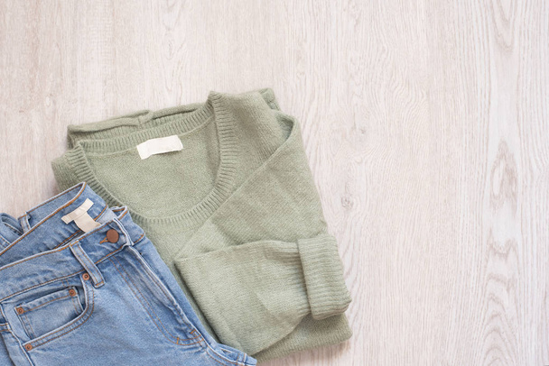 Women fashion clothes on wooden background. Flat lay female styled look. Sweater and jeans. Top view. Shopping Concept. Fashion Set Outfits - 写真・画像