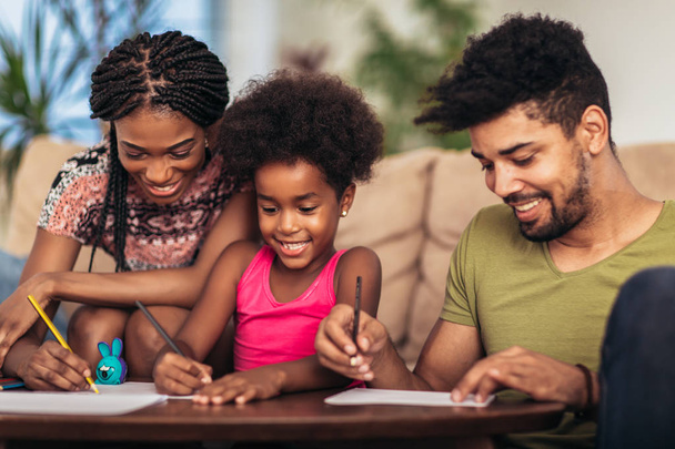 Äiti ja isä piirtävät tyttärensä kanssa. Afrikkalainen amerikkalainen perhe viettää aikaa yhdessä kotona
. - Valokuva, kuva