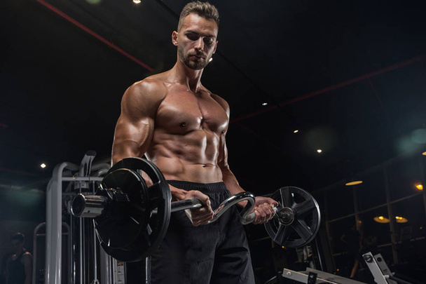 Muscular bodybuilder guy doing exercises with dumbbells in gym - Fotografie, Obrázek