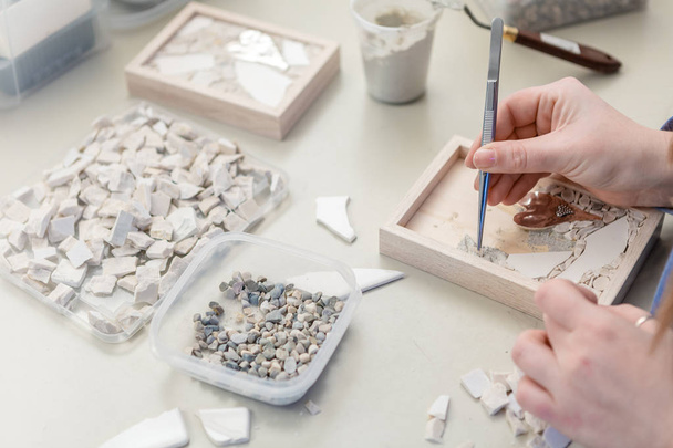 Handen van kunstenaar werken op kleine stenen mozaïek in haar atelier - Close up - Foto, afbeelding