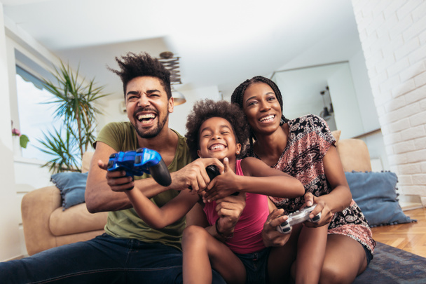 Smiling family sitting on the couch together playing video games - Foto, afbeelding