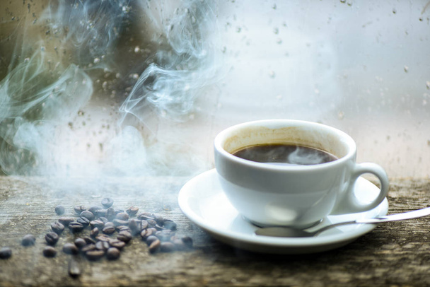 新鮮な醸造コーヒー ホワイト マグカップと窓辺の豆。ガラス窓とホット コーヒーのカップに濡れています。秋の曇り天気カフェイン飲むと良い。雨の日にコーヒーを楽しんでいます。コーヒーの朝の儀式 - 写真・画像