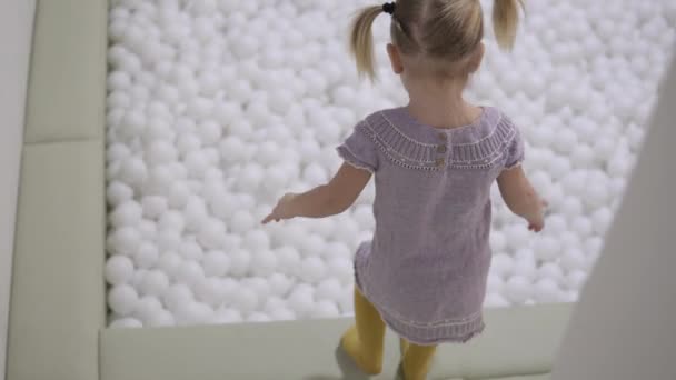 ein kleines Mädchen springt mit einem Haufen weißer Kugeln in einen Pool - Filmmaterial, Video