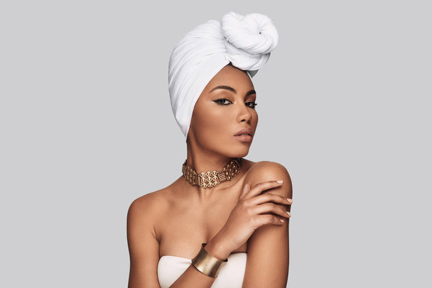 African style. Attractive young African woman in turban looking at camera while standing against grey background - Foto, immagini