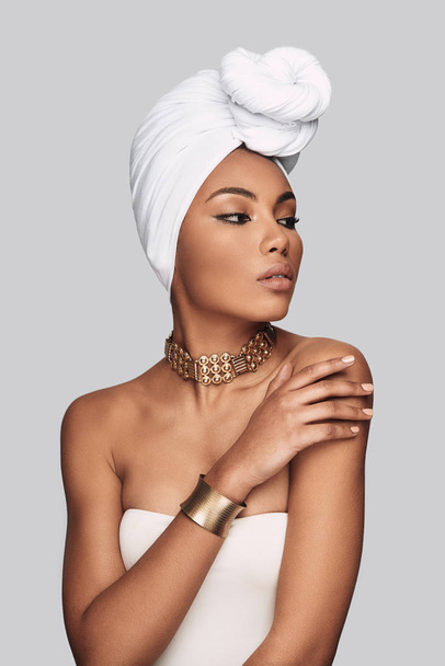 African beauty. Attractive young African woman in turban looking away while standing against grey background - Foto, imagen
